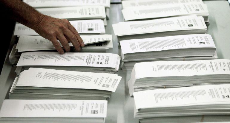 Un ciudadano coge una papeleta de una cabina en un colegio electoral