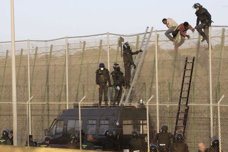 GRA019 MELILLA, 22/10/2014.- Agentes de Policía junto a a algunos de los ochenta inmigrantes que están encaramados desde primera hora a la valla de Melilla, fronteriza con Marruecos, tras el último intento de entrar en la ciudad autonóma protagonizado por