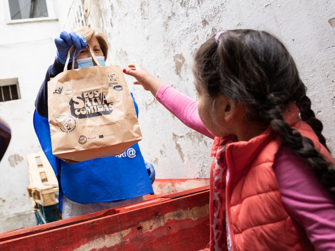 Imagen de una voluntaria de `Los salvacomidas´entregando un menú saludable a una niña