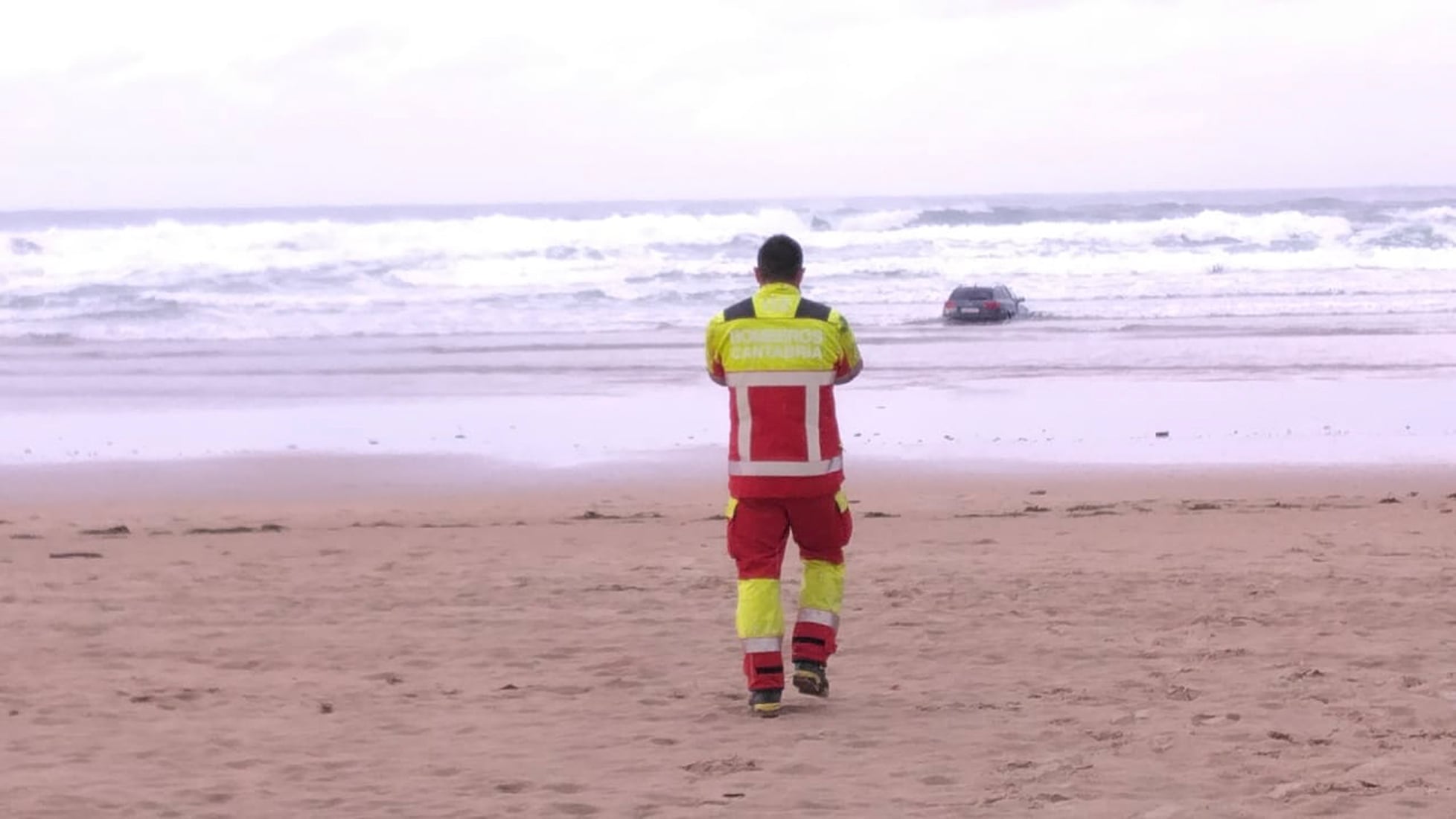 Un efectivo de los Bomberos de Cantabria se dirige hacia un coche encallado, dentro del agua, en la orilla de la playa de Oyambre.