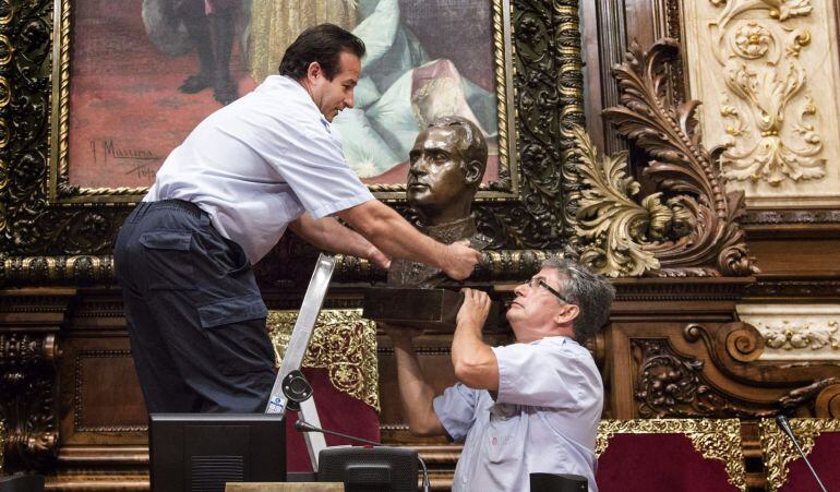 Dos operarios municipales retiran el busto del Rey Juan Carlos I del salón en el que se celebran los plenos municipales del Ayuntamiento de Barcelona. 