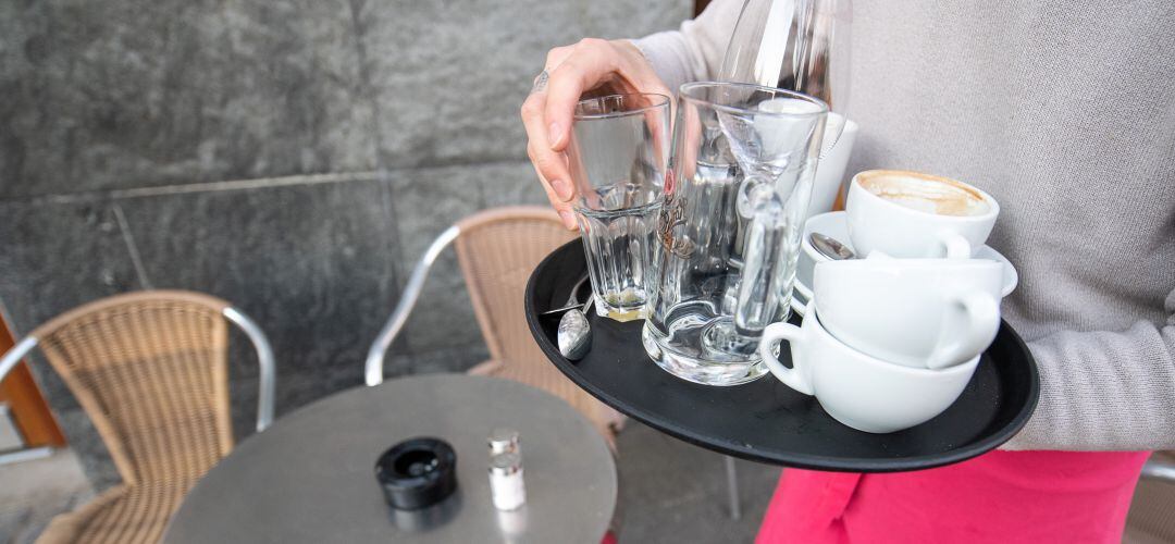 Un profesional de la hostelería recoge vasos y tazas de la mesa de una terraza