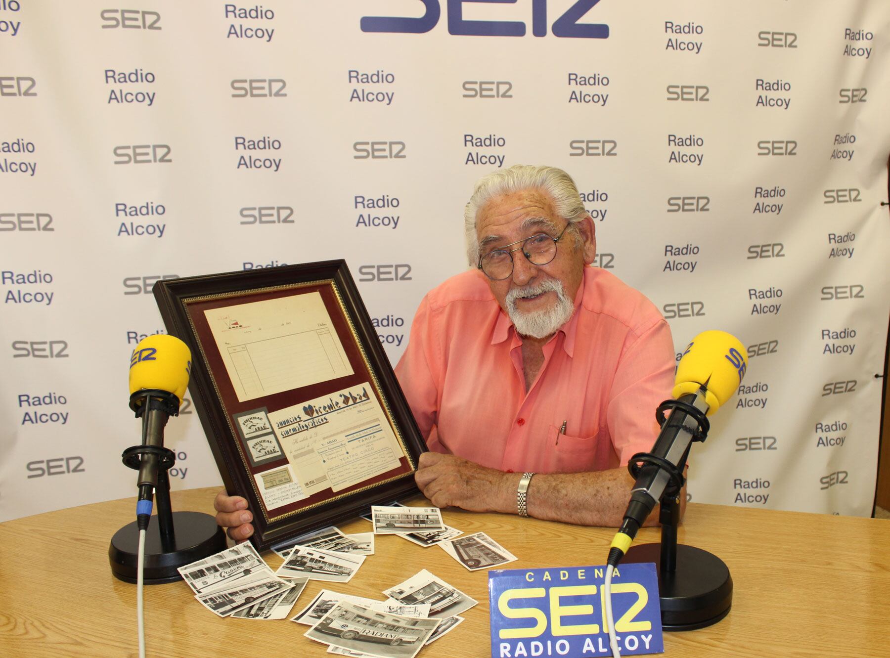 Rafael Abad i Segura, en l'estudi central de Radio Alcoy amb fotos antigues de l'autobús i el billet emmarcat