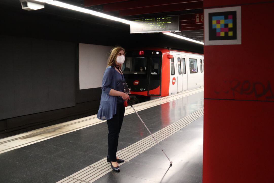 Una dona amb discapacitat visual esperant el metro al costat d'una etiqueta intel·ligent a l'estació de metro de Plaça Universitat