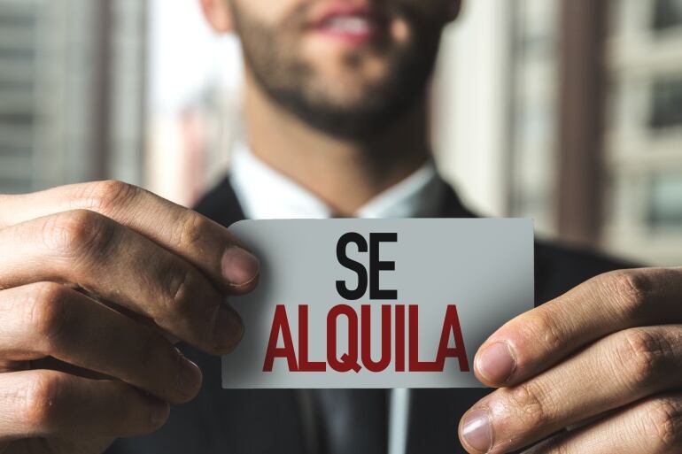 Un hombre sostiene un pequeño cartel de alquiler