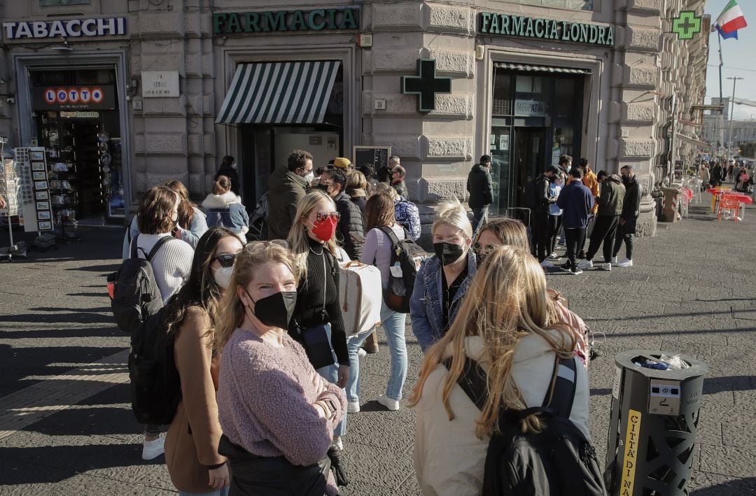 Gente fuera de una farmacia llevando mascarilla.