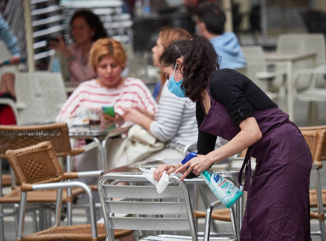 Una trabajadora desinfecta las mesas y sillas de una terraza