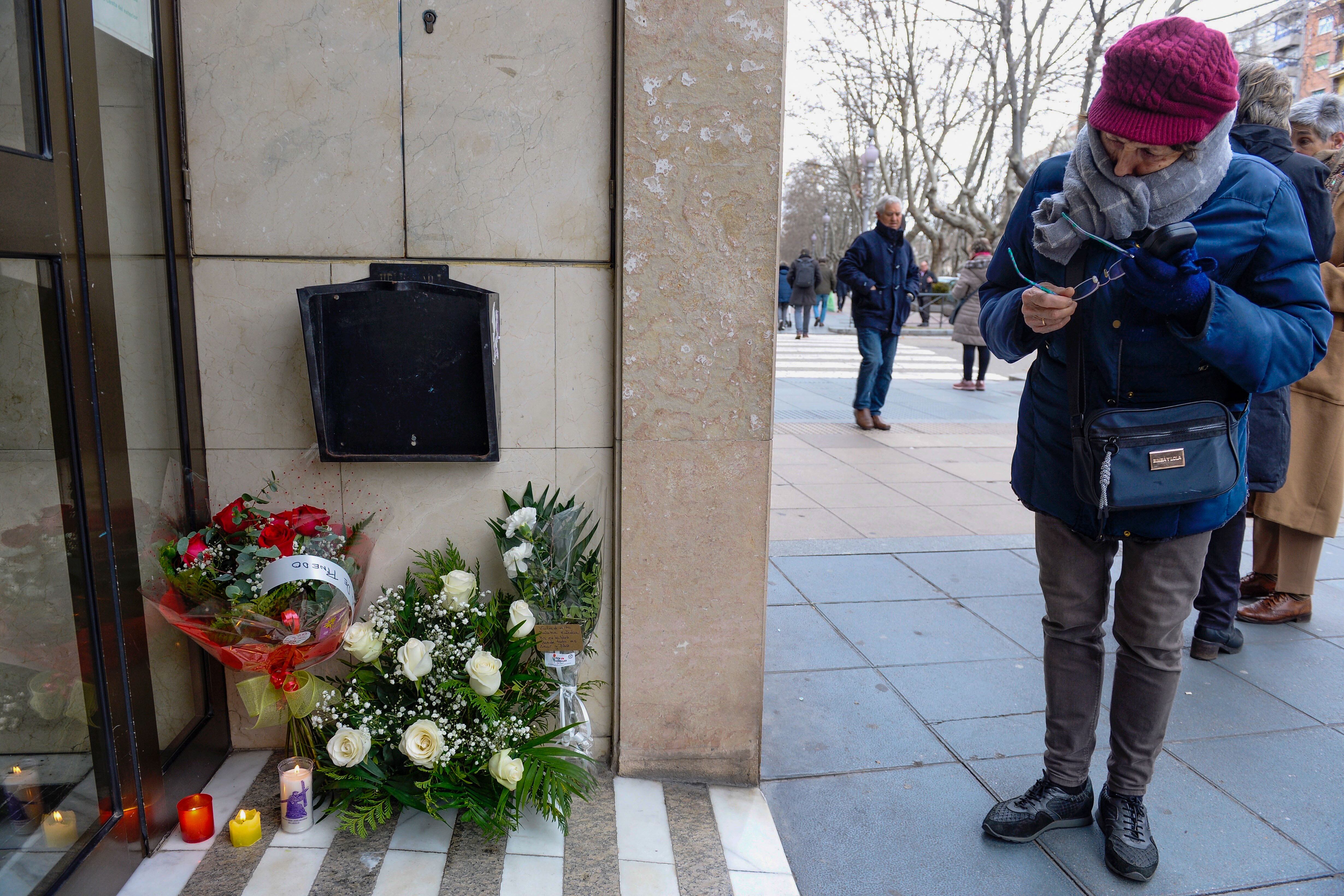 Una mujer observa las flores y velas colocadas en el portal del inmueble en el que un hombre mató a su novia y la hija de esta en Valladolid.