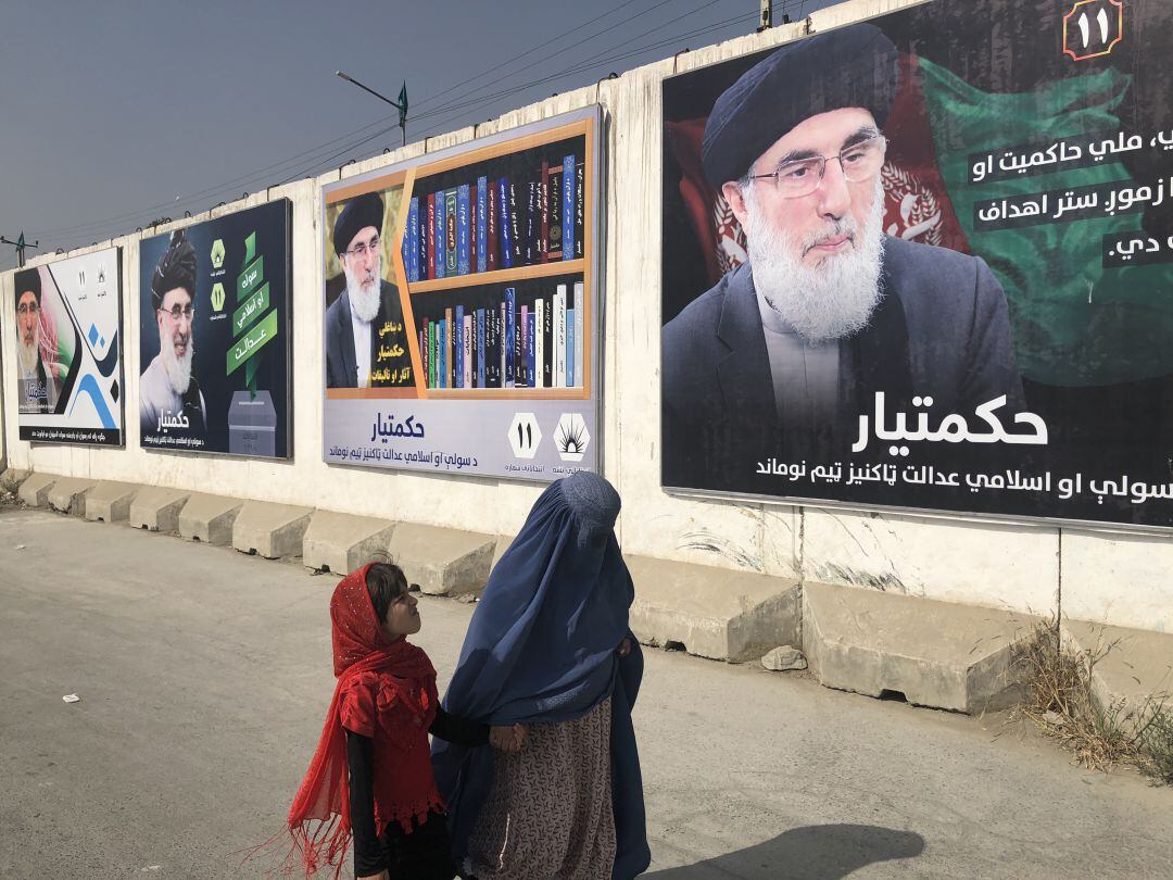 Una mujer con burka y una niña pasan por un muro con publicidad electoral del señor de la guerra Gulbudin Hekmatyar