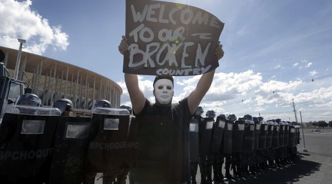 Un joven sostiene una pancarta frente a un grupo de agentes de policía antidisturbios, durante una protesta llevada a cabo horas antes del partido de Copa Confederaciones 2013 entre las selecciones de Brasil y Japón, en las inmediaciones del Estadio Nacio