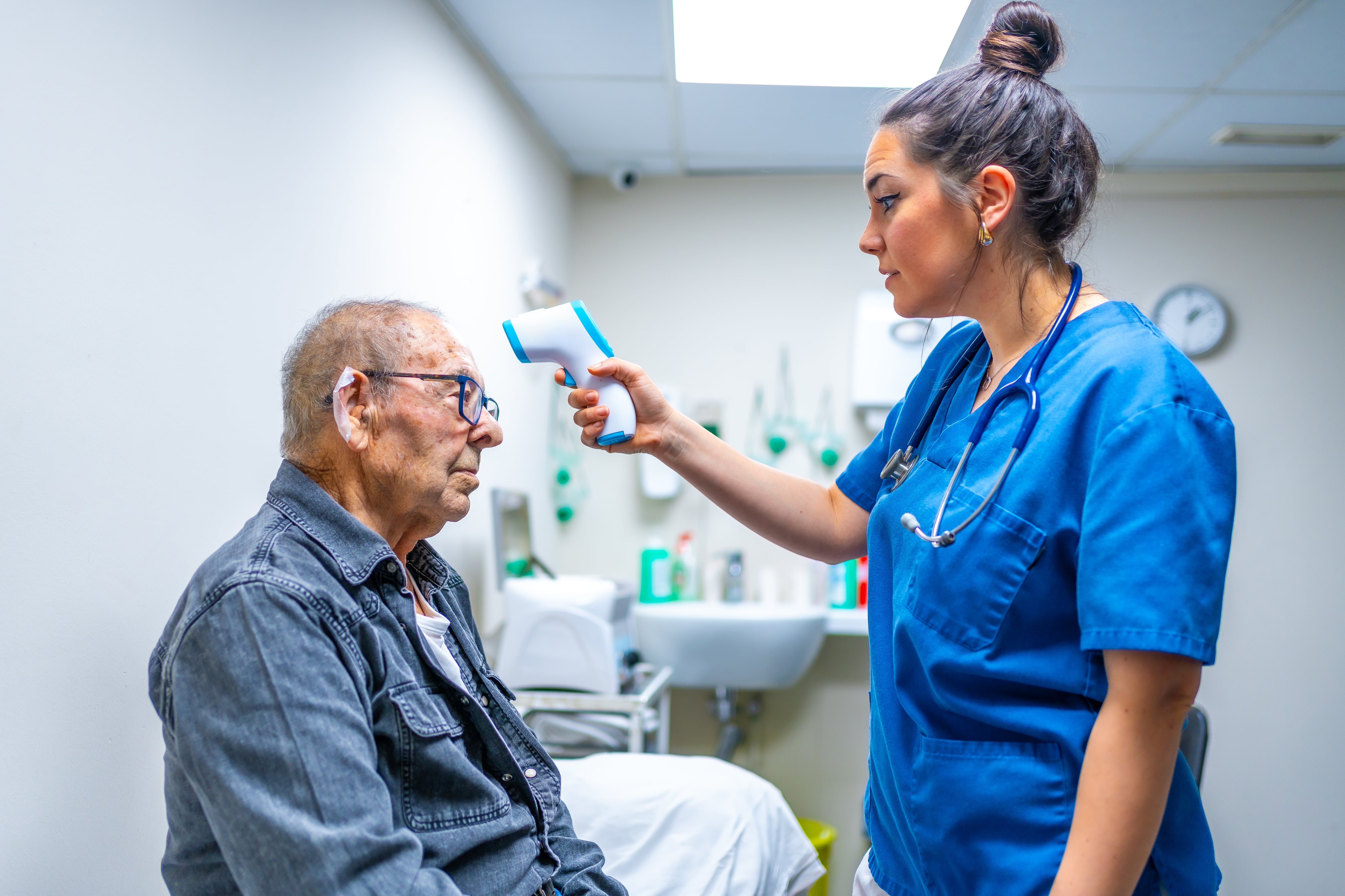Nurse is using a digital thermometer to take the temperature of a senior man in a geriatrics