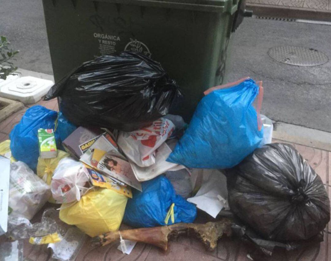 Contenedor de basura rodeado de residuos