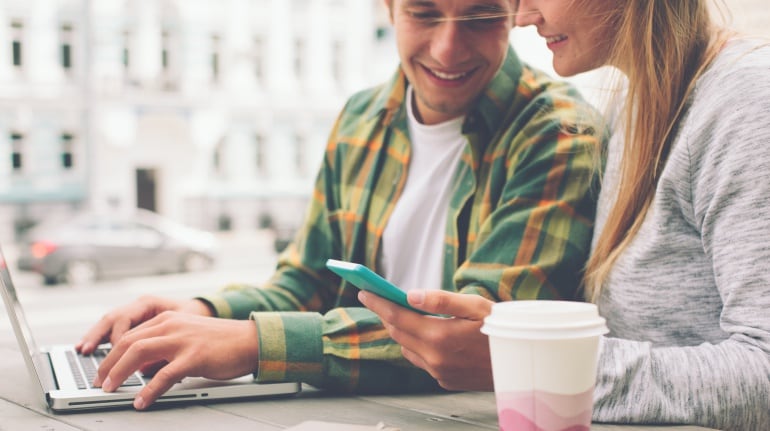 Imagen de un chico con un ordenador y una chica con un teléfono inteligente.