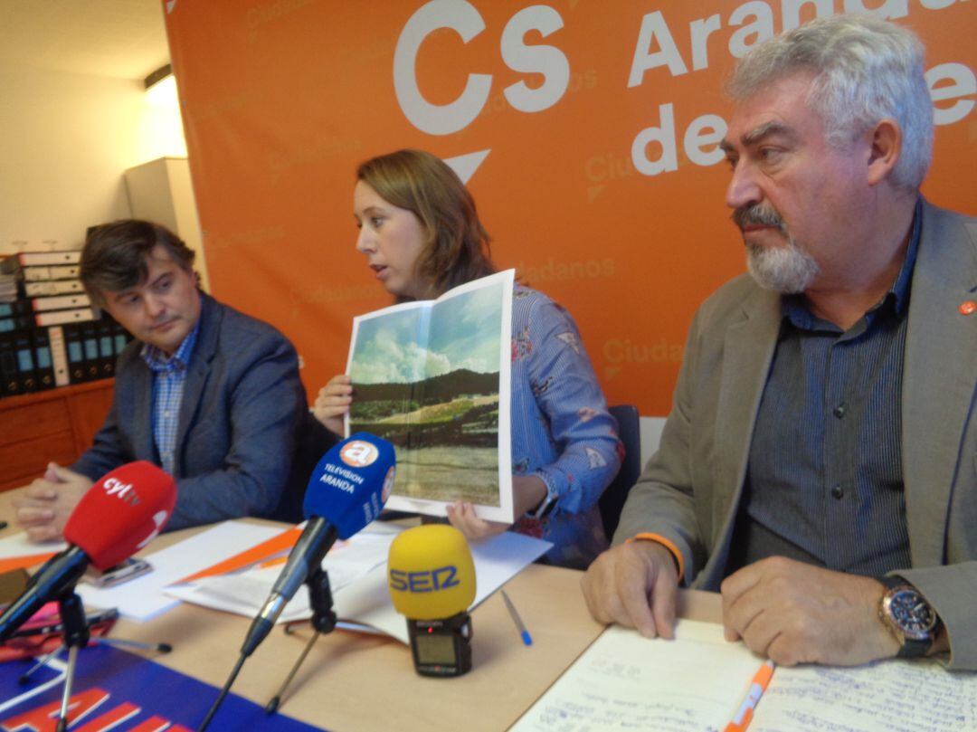 La candidata al Congreso por Burgos muestra a la prensa la foto del camión calcinado abandonado en la N-122, acompañada del procurador regional (dcha) y del portavoz municipal del partido, Francisco Martín