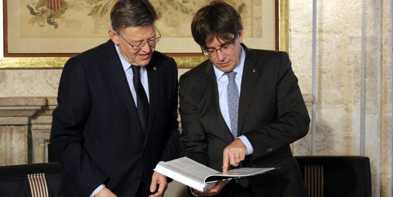 Carles Puigdemont i  Ximo Puig mostrant el llibre &#039;La pervivència de la nació&#039;, regal del president al cap de govern de la Generalitat Valenciana. 