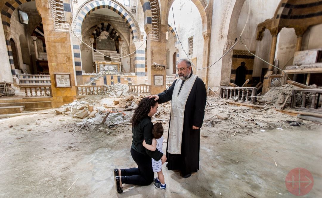 Un sacerdote sirio consuela a una familia cristiana en una iglesia afectada por la guerra.