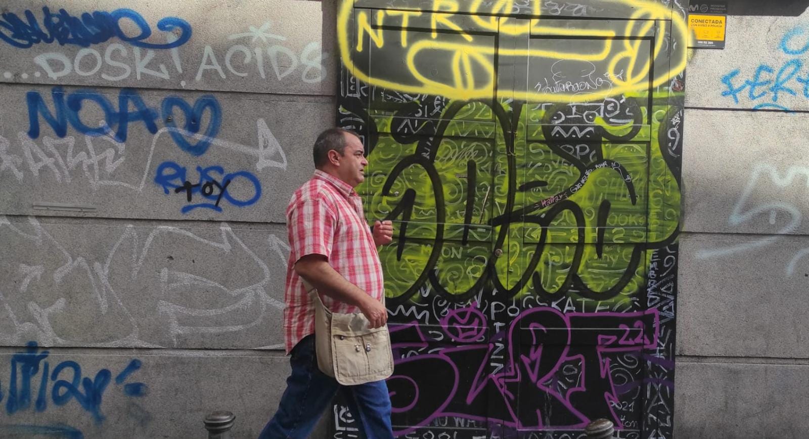 Un viandante pasa por delante de una fachada en Madrid llena de grafiti