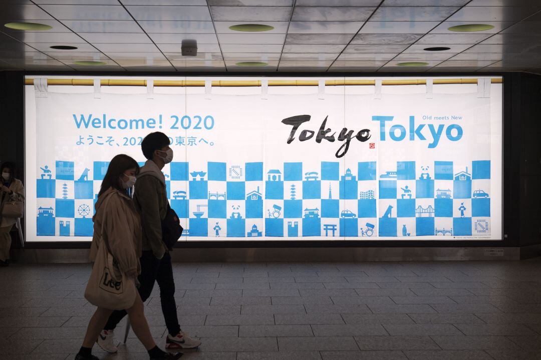 Dos personas pasan por delante de un cartel de los Juegos de Tokio.