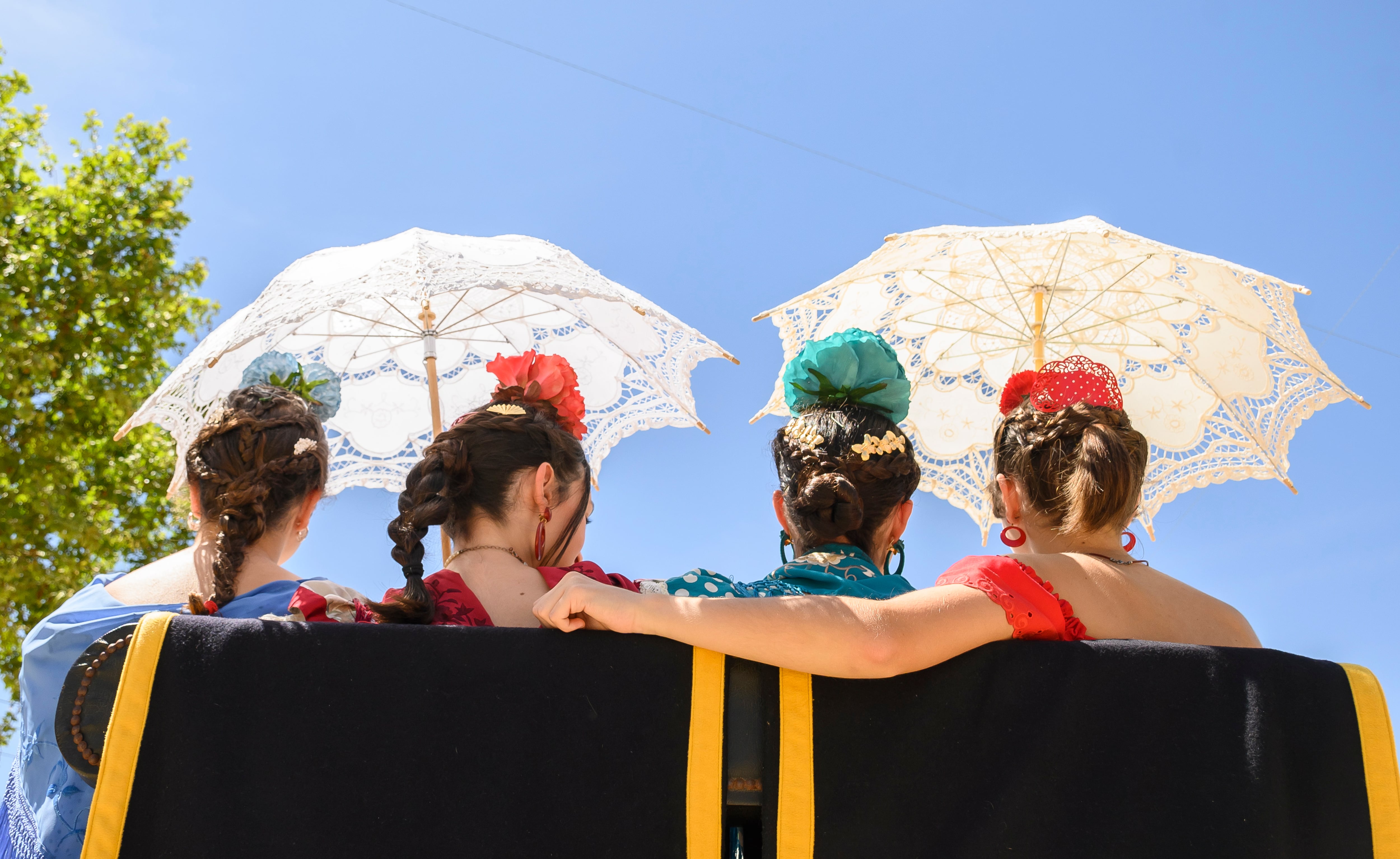 Unas jóvenes pasean en coche de caballos mientras se resguardan con dos sombrillas por las altas temperaturas que se están registrando estos días, en la Feria de Abril de Sevilla. EFE/Raúl Caro