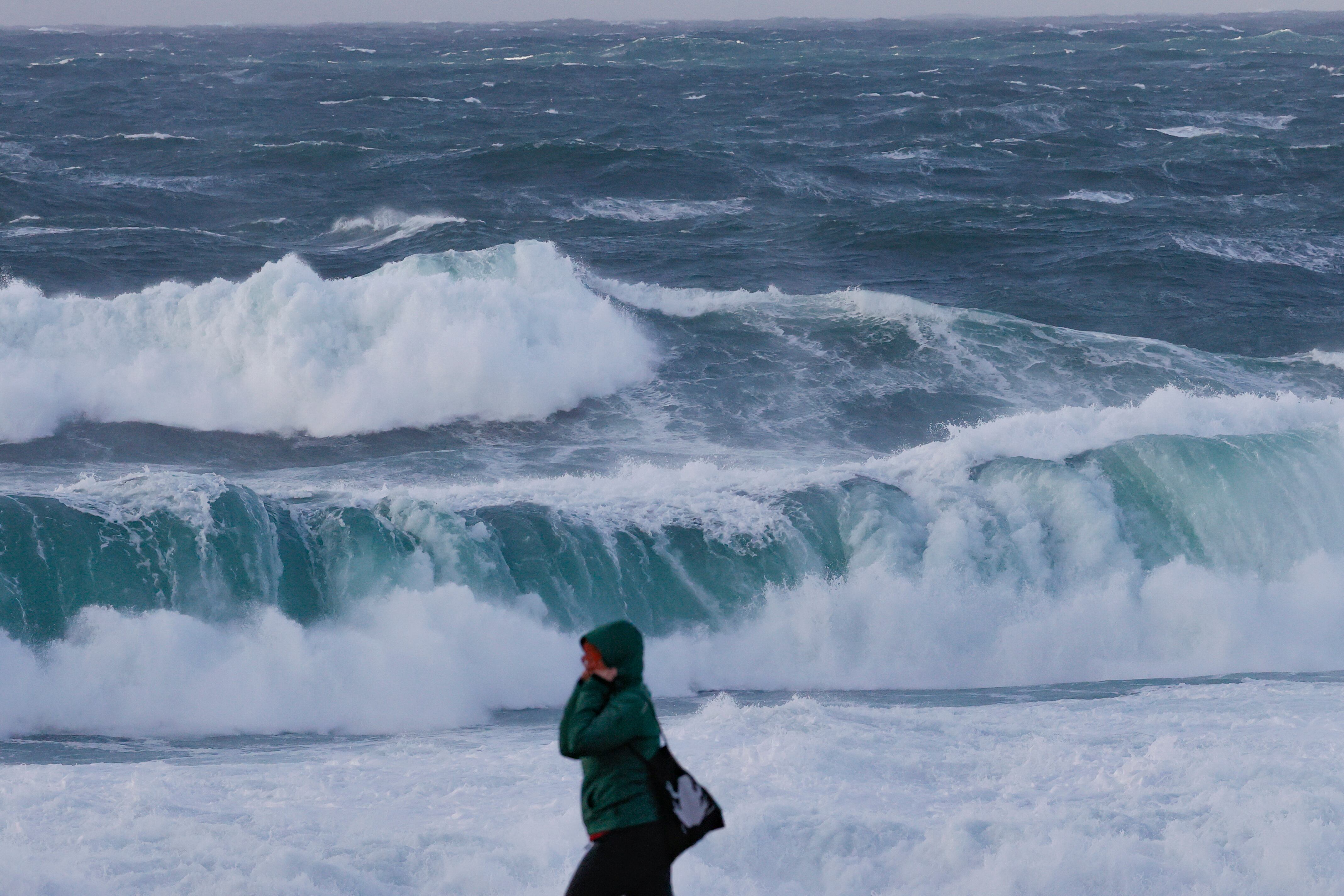 MUXÍA(A CORUÑA), 17/01/2023.-Un apersona camina delante del fuerte oleaje esta tarde en la costa de Muxía, en la Costa da Morte. Tras el paso ayer lunes de la borrasca Gérard, la parte más adversa de este temporal invernal corresponderá a la borrasca Fien, que a partir de este martes mantiene activado el aviso rojo en Galicia por olas de 9 metros y en otras 12 comunidades en naranja por nieve en cotas bajas, lluvias y fuerte viento. EFE/Lavandeira jr