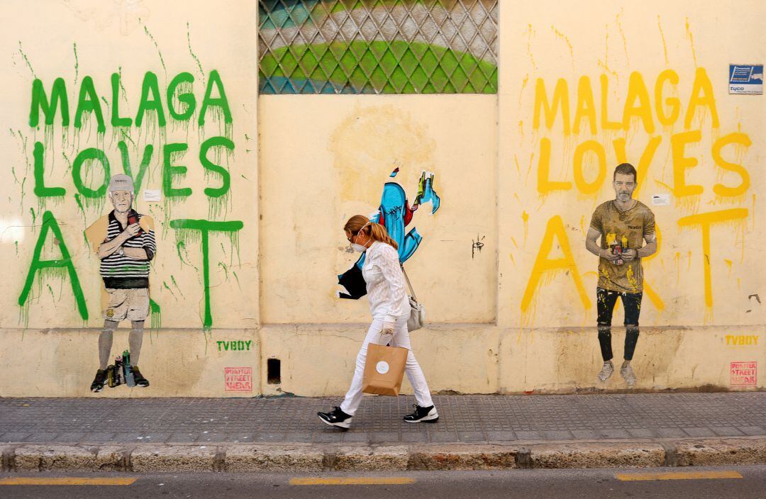 A woman wearing a protective face mask walks past graffiti depicting Pablo Picasso and Antonio Banderas, amid the coronavirus disease 