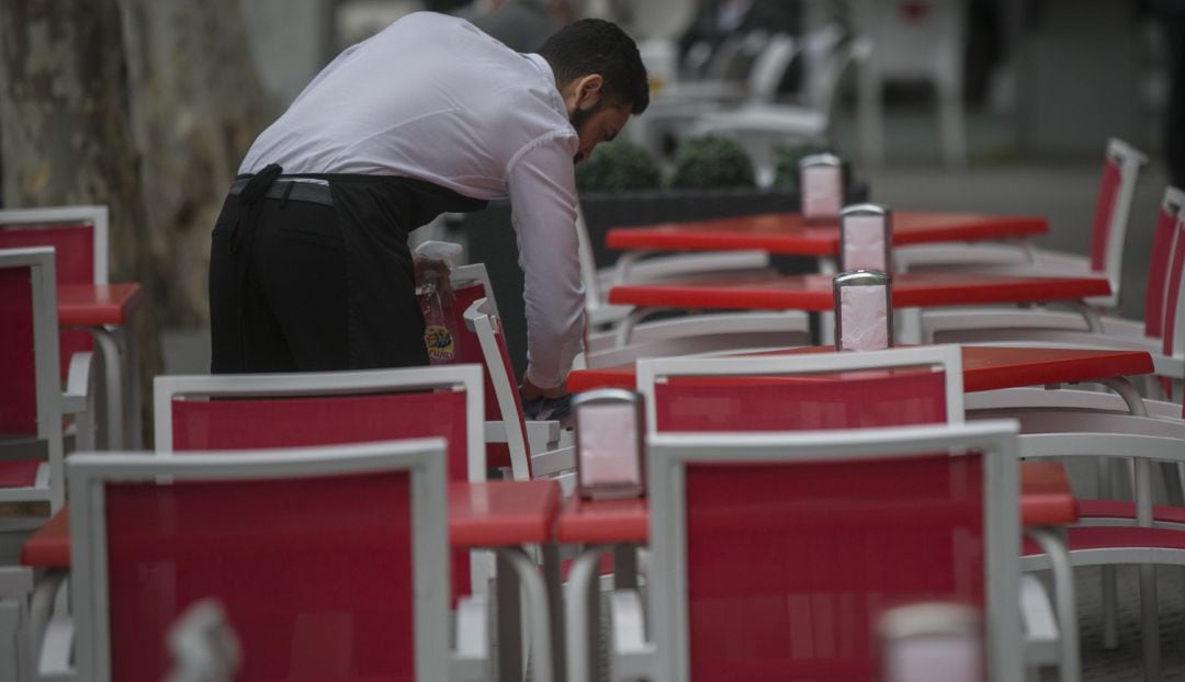 Un camarero limpia las mesas de una terraza.