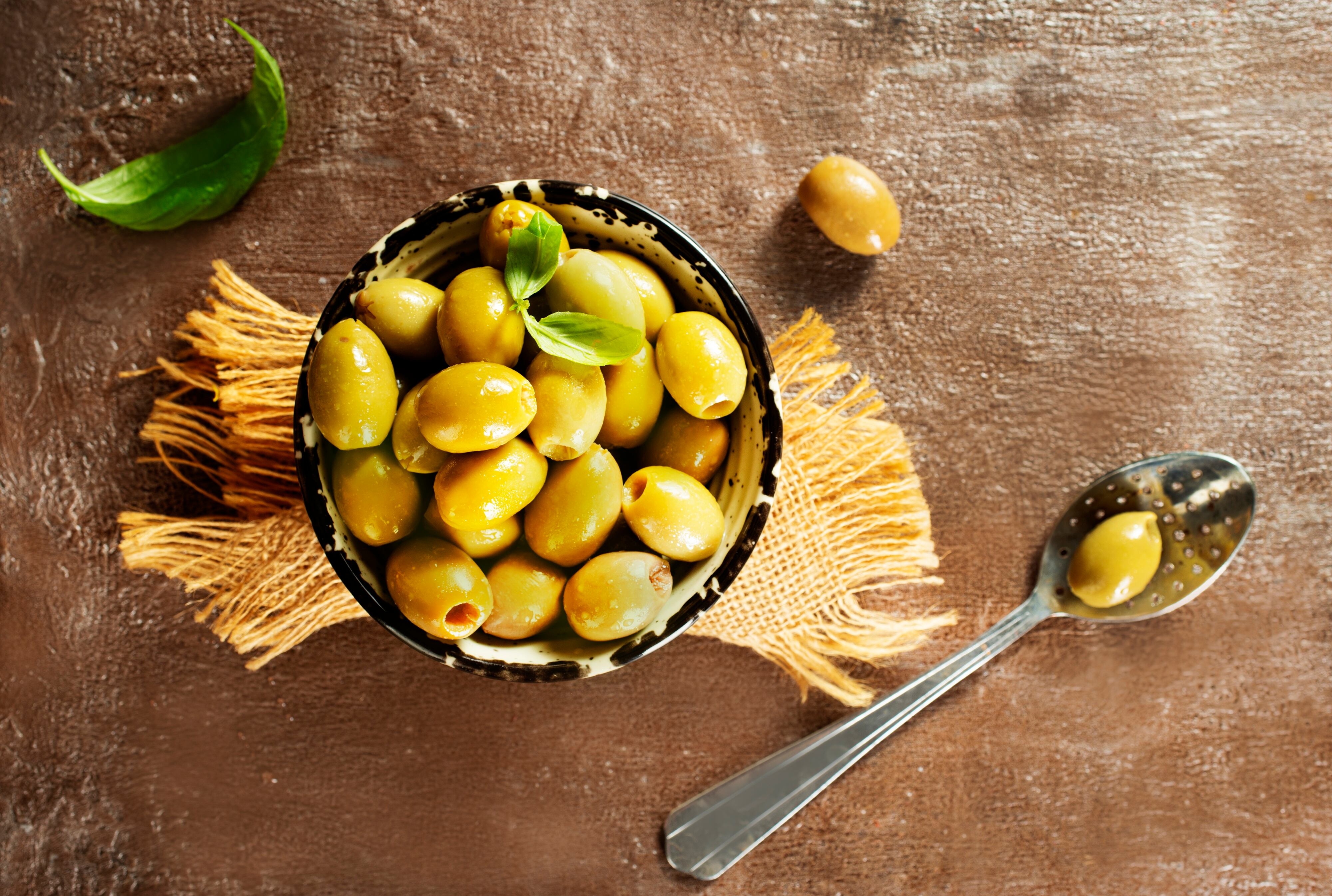 Green olives and basil leaves on wooden background