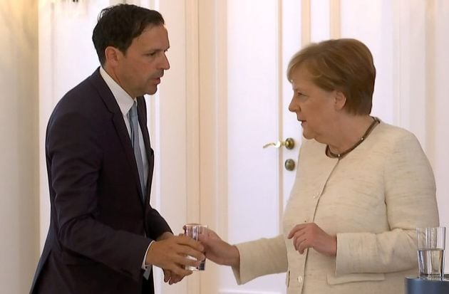 Un colaborador de Angela Merkel ofrece un vaso de agua a la canciller.