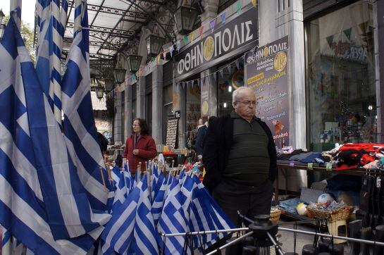 Un ciudadano camina junto a una tienda que vende banderas griegas.