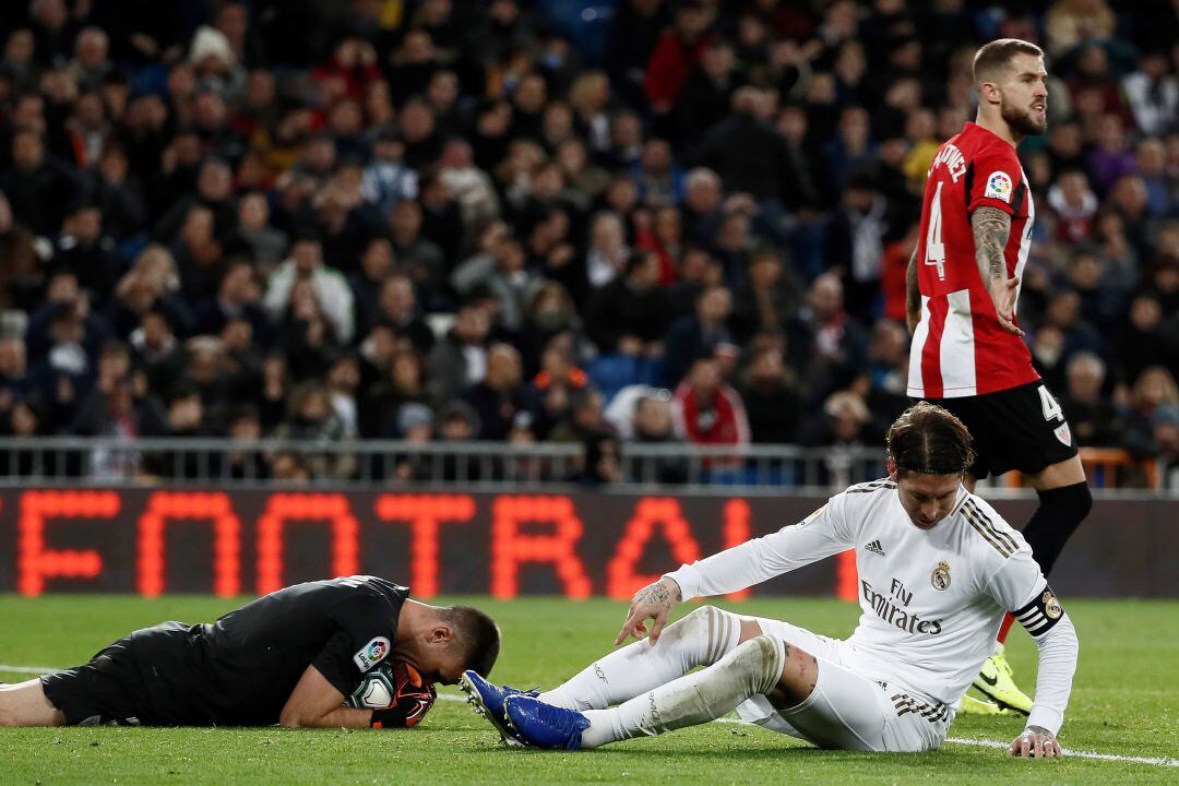 El portero del Athletic de Bilbao Unai Simón (i) atrapa un balón ante Sergio Ramos (c), del Real Madrid, durante el partido de Liga en Primera División que disputan esta noche en el estadio Santiago Bernabéu
