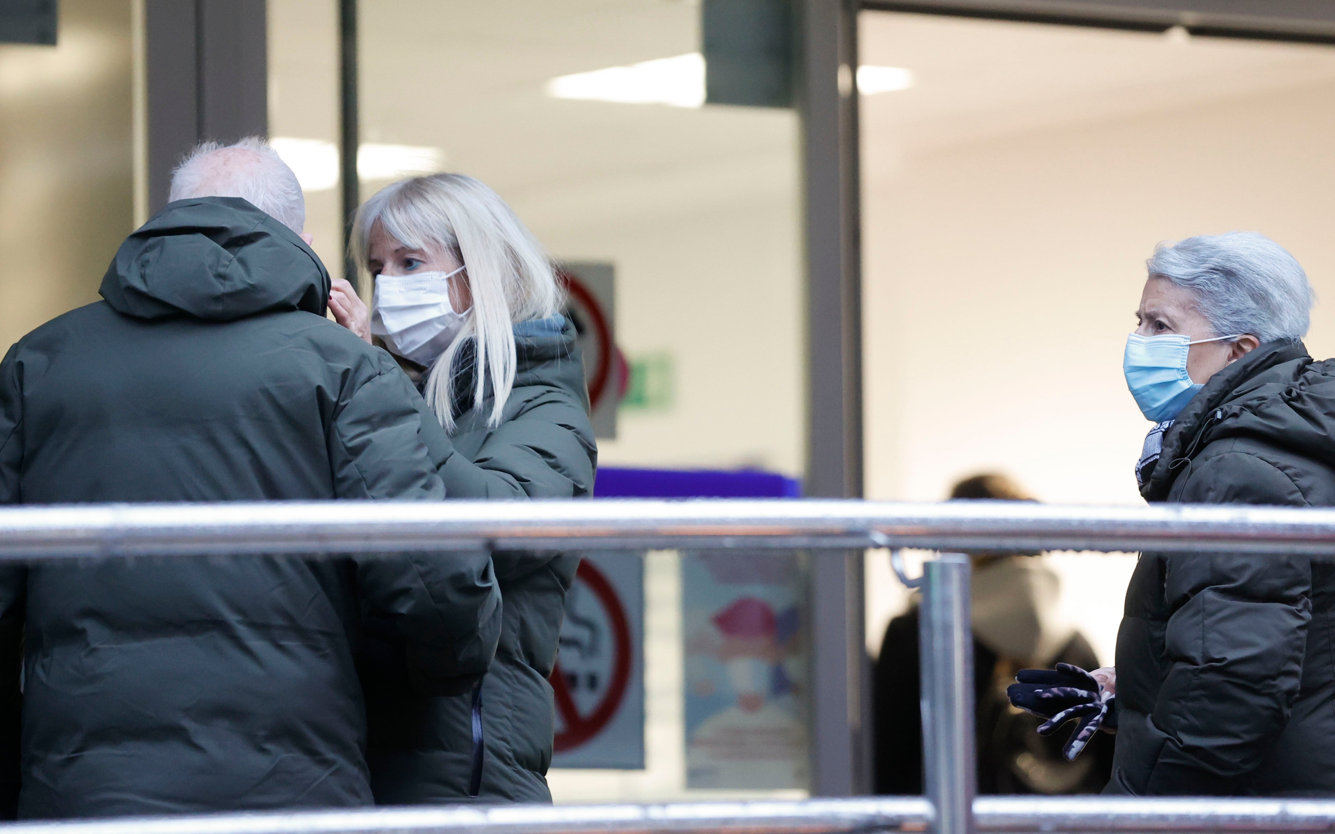 Una hija coloca una mascarilla a su padre en presencia de su madre al entrar en un centro de salud.