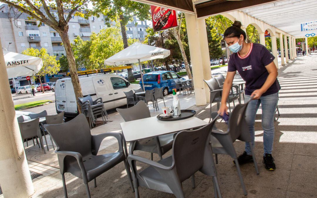 Una camarera limpia una de las mesas de la terraza del bar en el que trabaja