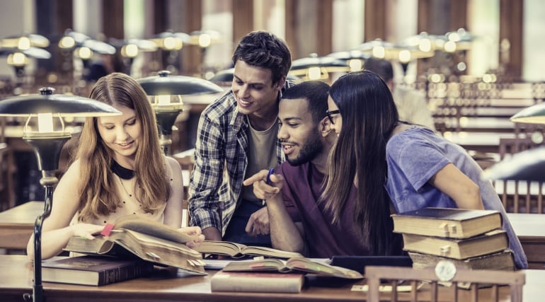 Cuatro jóvenes estudian en una biblioteca.