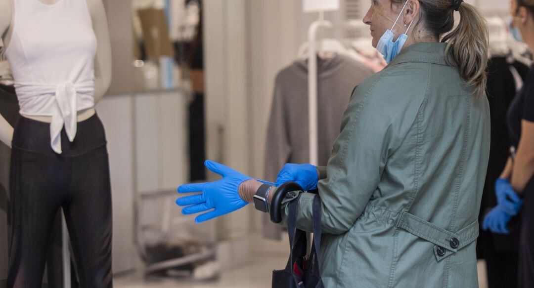 Una mujer se coloca unos guantes proporcionados por el establecimiento al entrar en una tienda de ropa.