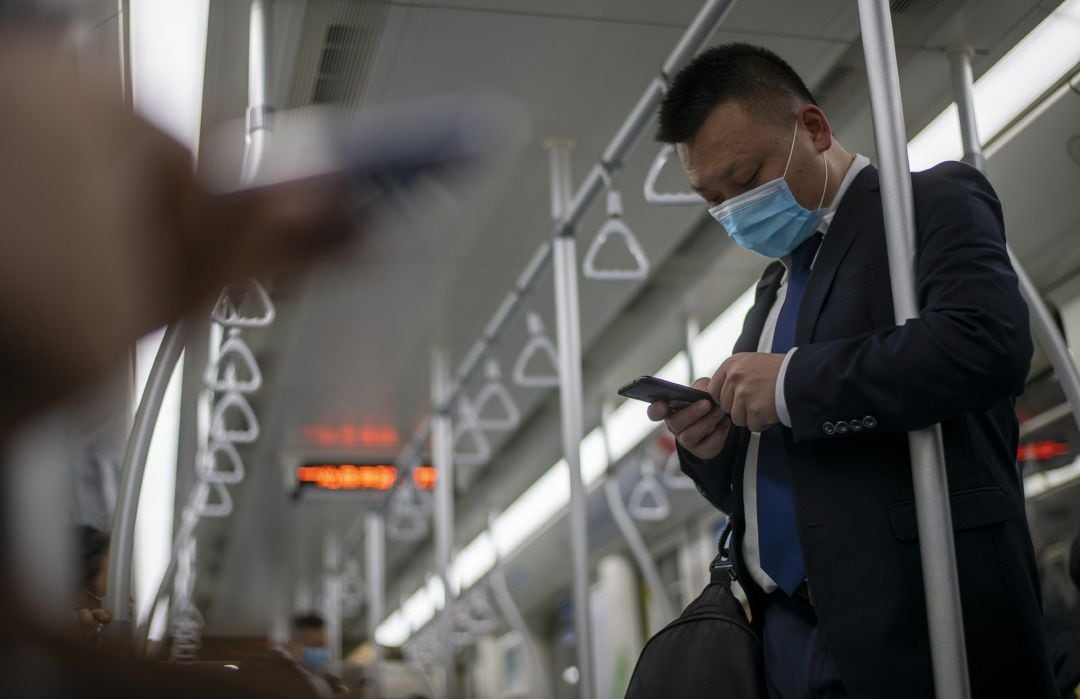 Un hombre protegido con mascarilla se apoya en la barra de un vagón de metro mientras utiliza su teléfono móvil sin guantes en la ciudad de Shanghái (China).