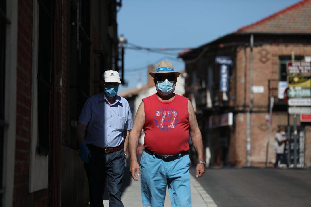 Dos hombres protegidos con mascarilla andan por una calle del pueblo madrileño de Algete.
