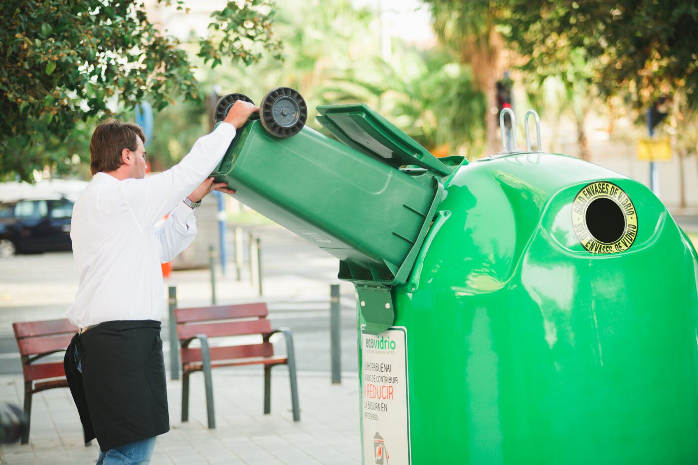 Un camarero tira envases de vidrio en el contenedor específico.