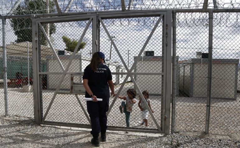 Una agente de policía conversa con dos niñas refugiadas iraquíes al otr lado de la valla en el centro de detención de inmigrantes indocumentados de Amygdaleza, en Atenas