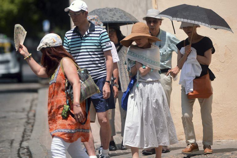 Un grupo de turistas se tapan con sombrillas o con pañuelos para seguir su visita por Córdoba.