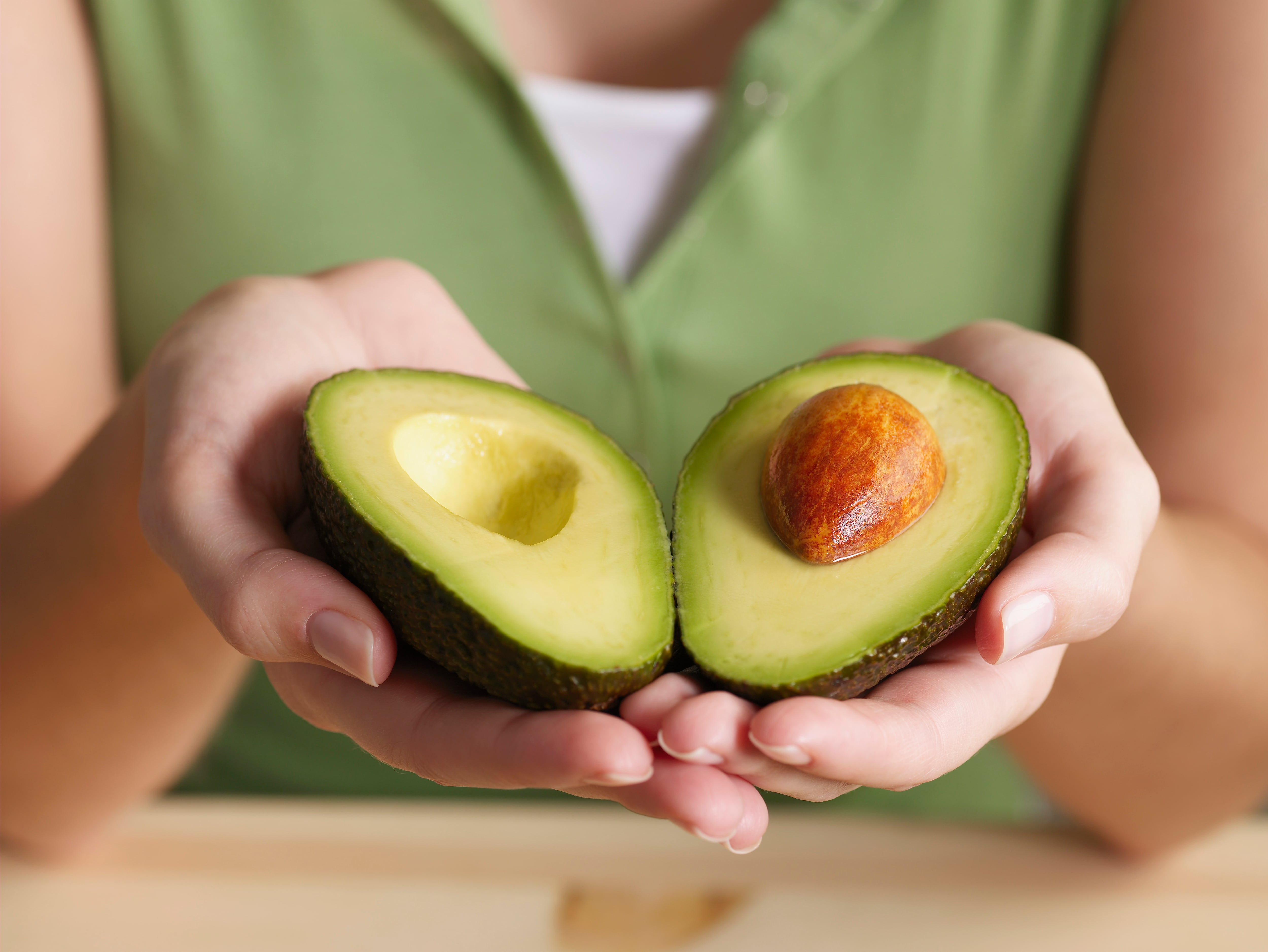 Una mujer sostiene las dos mitades de un aguacate.