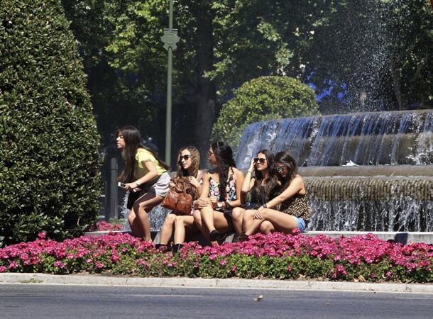 Un grupo de chicas se refrescan frente a la fuente de Neptuno ante las altas temperaturas.