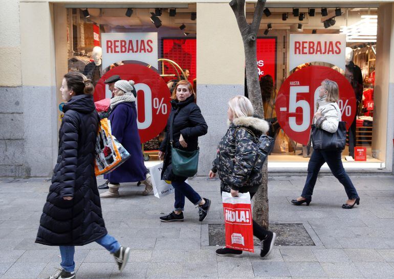 Varias personas pasean frente a un escaparate que anuncia las rebajas de invierno 2018