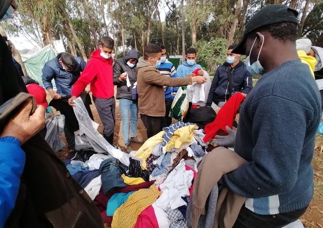 Un grupo de personas recogen algo de ropa colocada en el exterior del campamento de Las Raíces sobre una lona