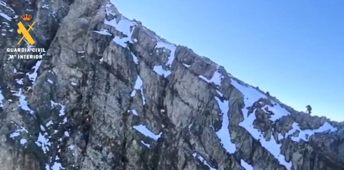Un Guardia Civil asciende por la montaña, mientras hay dos montañeros enriscados
