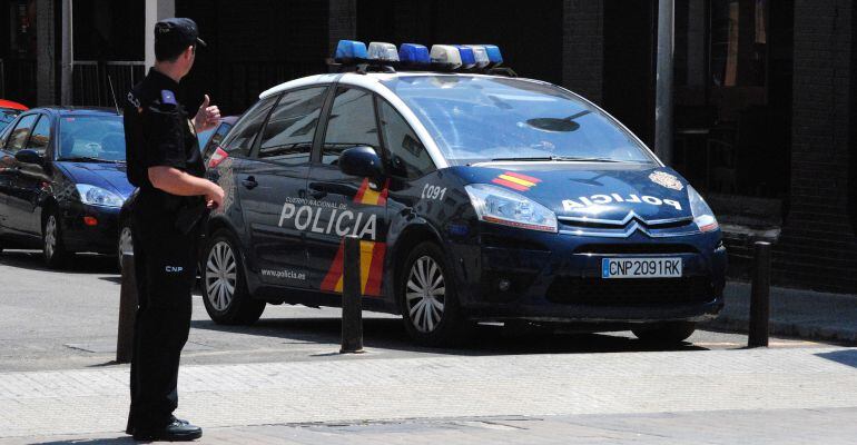 Agente del Cuerpo Nacional de Policía junto a un vehículo policial