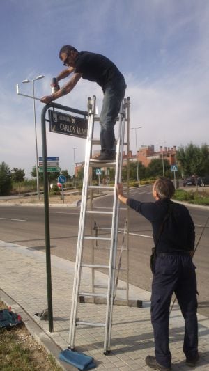 Dos operarios colocan la placa con el nombre de Carlos Llamas en una glorieta en Canillejas.