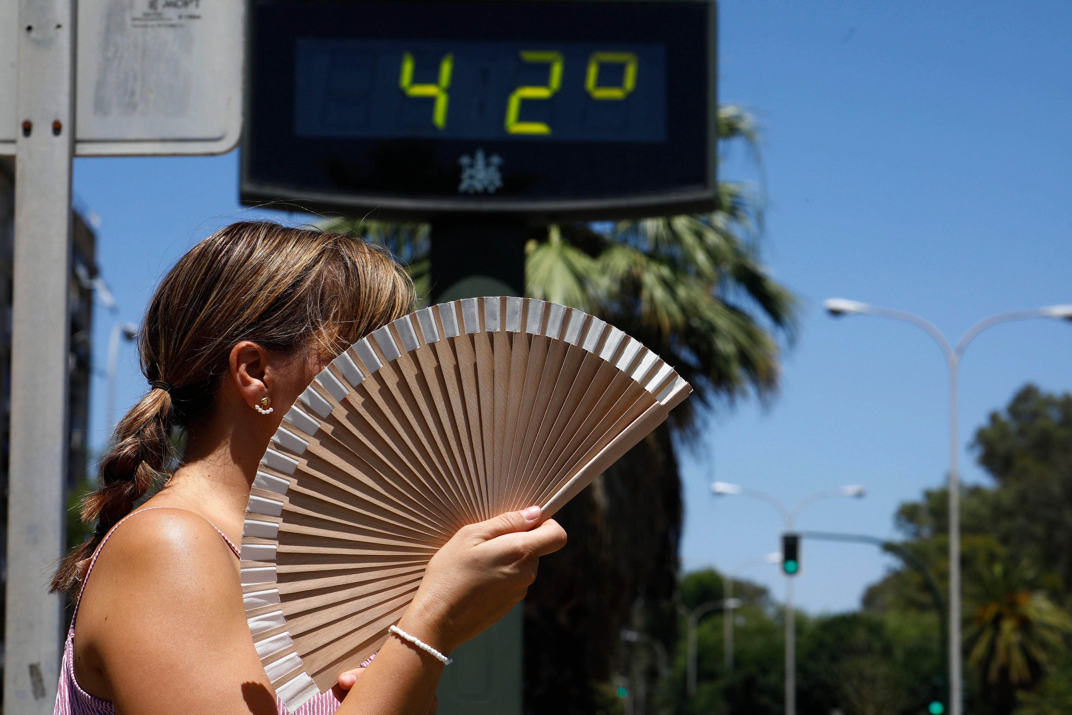 Una mujer se abanica mientras pasa por un termómetro de calle que marca 42 grados en Córdoba.