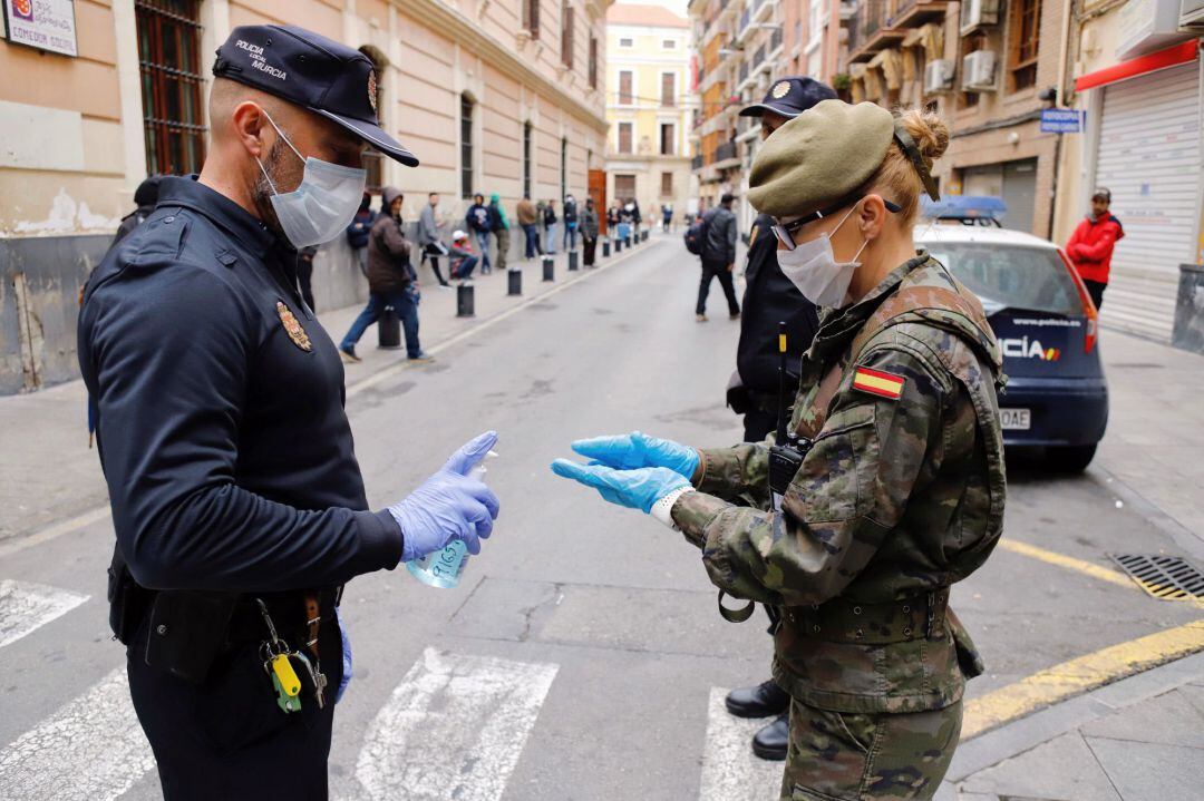 Un Policía Local de Murcia, ofrece gel desinfectante a una militar del Ejército de Tierra