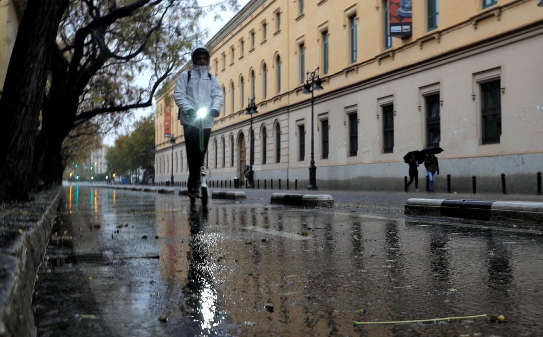 Una persona circula bajo la lluvia, en un patinete eléctrico en una calle de Valencia. 