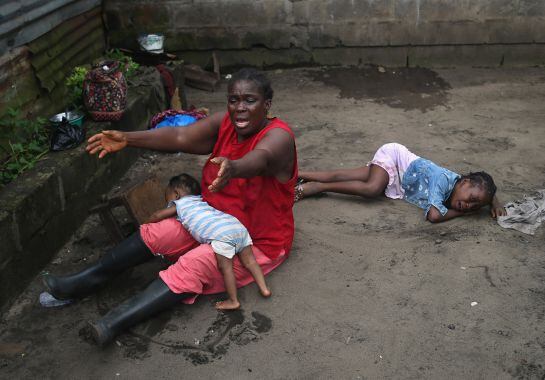 MONROVIA, LIBERIA - OCTOBER 10: Sophia Doe sits with her grandchildren Beauty Mandi, 9 months (L) and Arthuneh Qunoh, 9, (R), while watching the arrival an Ebola burial team to take away the body of her daughter Mekie Nagbe, 28, for cremation on October 1